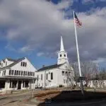 A white church in New Hampshire with a flag flying over it.